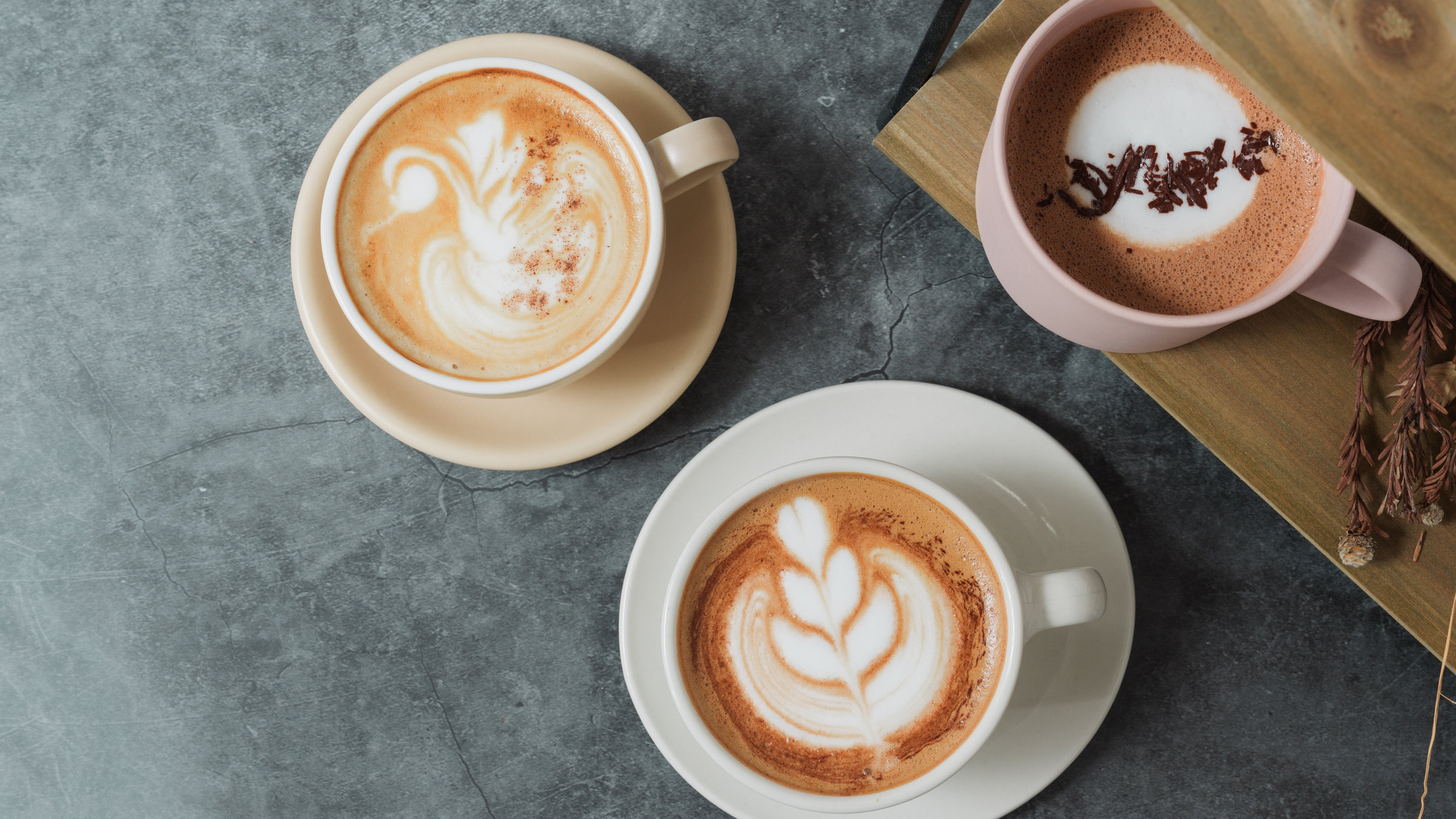 石のテーブルに並べた、ラテアートのカフェラテ2杯とカカオのドリンク